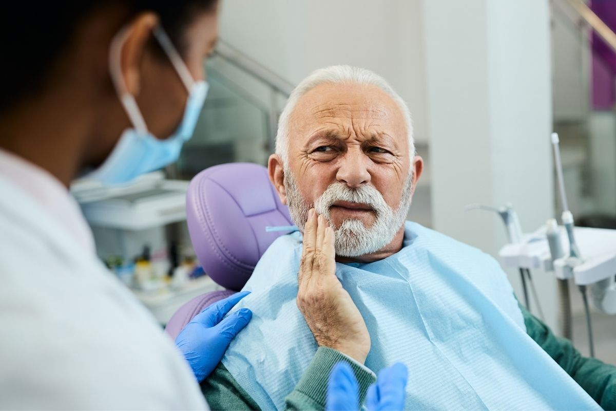 Senior man experiencing tooth pain during dental examination with dentist.
