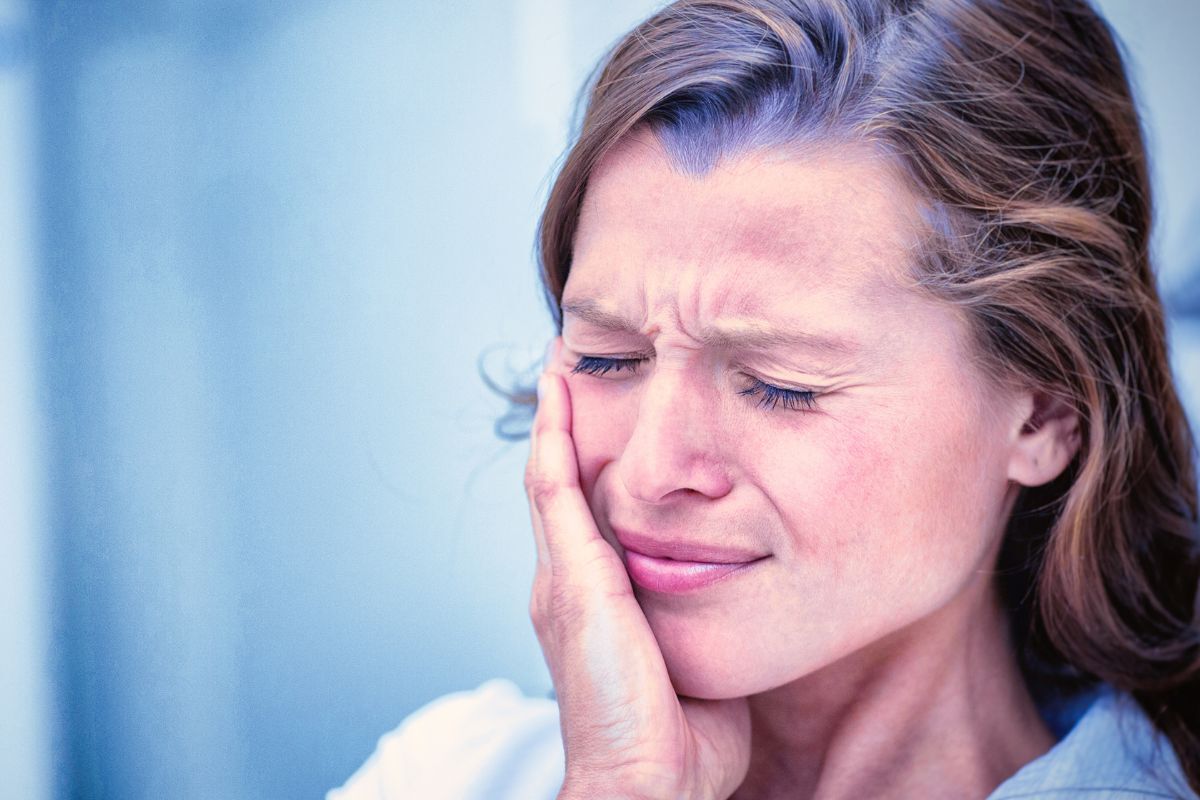 Woman holding her cheek in pain, showing signs of a tooth abscess requiring urgent dental care.