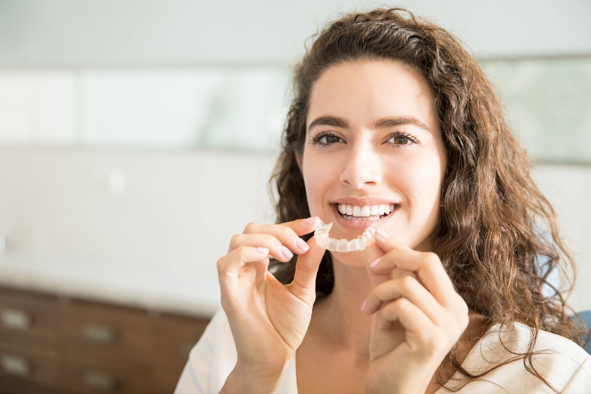 Young woman inserting clear aligner tray for Invisalign teeth straightening treatment.